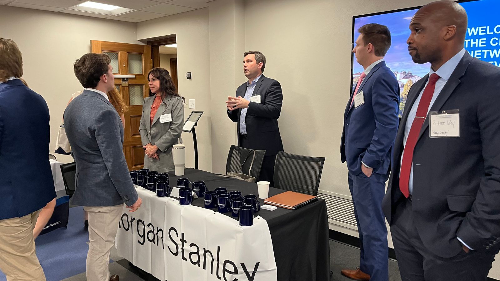 Students speaking with Morgan Stanley professionals over an information table at a career networking event, with branded mugs