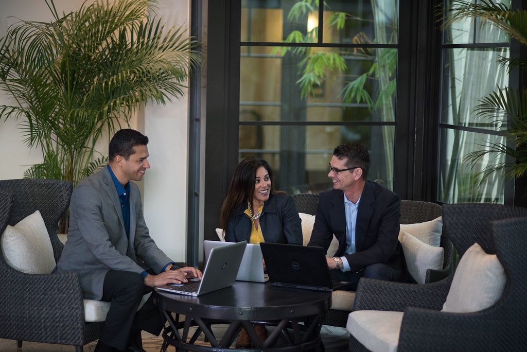 Three Rollins MBA students or Crummer faculty or staff members sit in a relaxed sitting area at a coffee table with a laptop