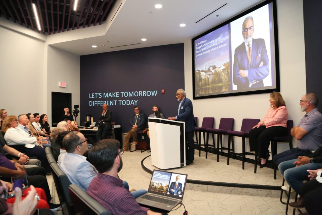 Rollins Crummer Dean speaks at podium during MBA event with an audience and presentation screen in a modern lecture hall