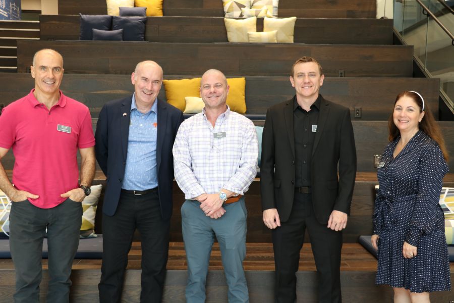 Five professionals and a student stand in front of tiered seating with pillows in modern lounge area at Rollins College