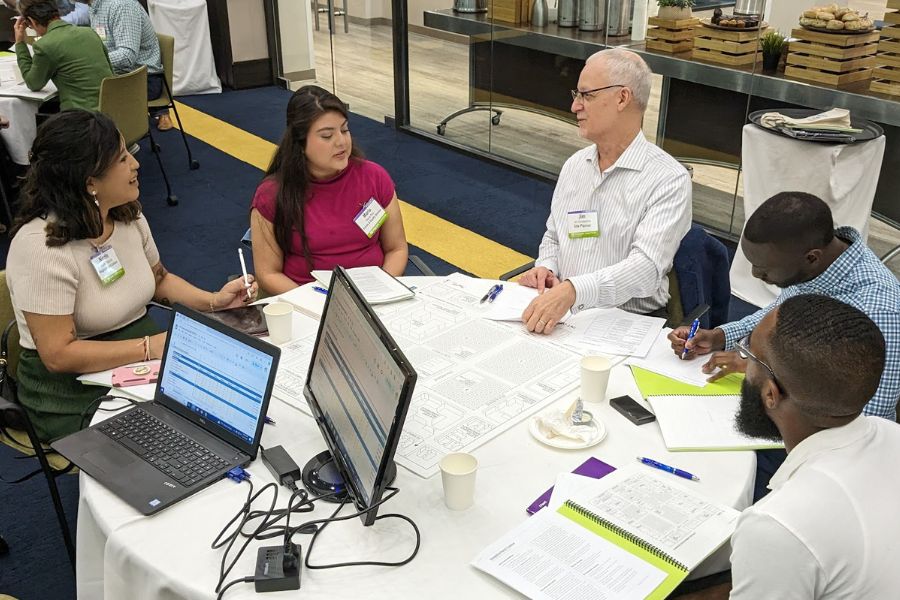 Crummer executive education students engaged in a group discussion at small table with professor with laptops and documents