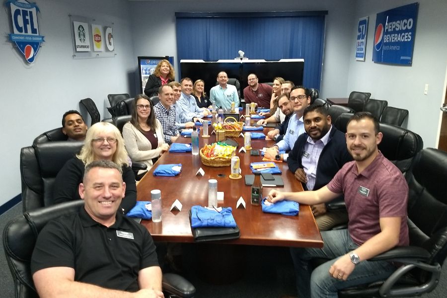 Around a conference table with snacks and nametags, a group of business professionals turn towards the camera and smile.