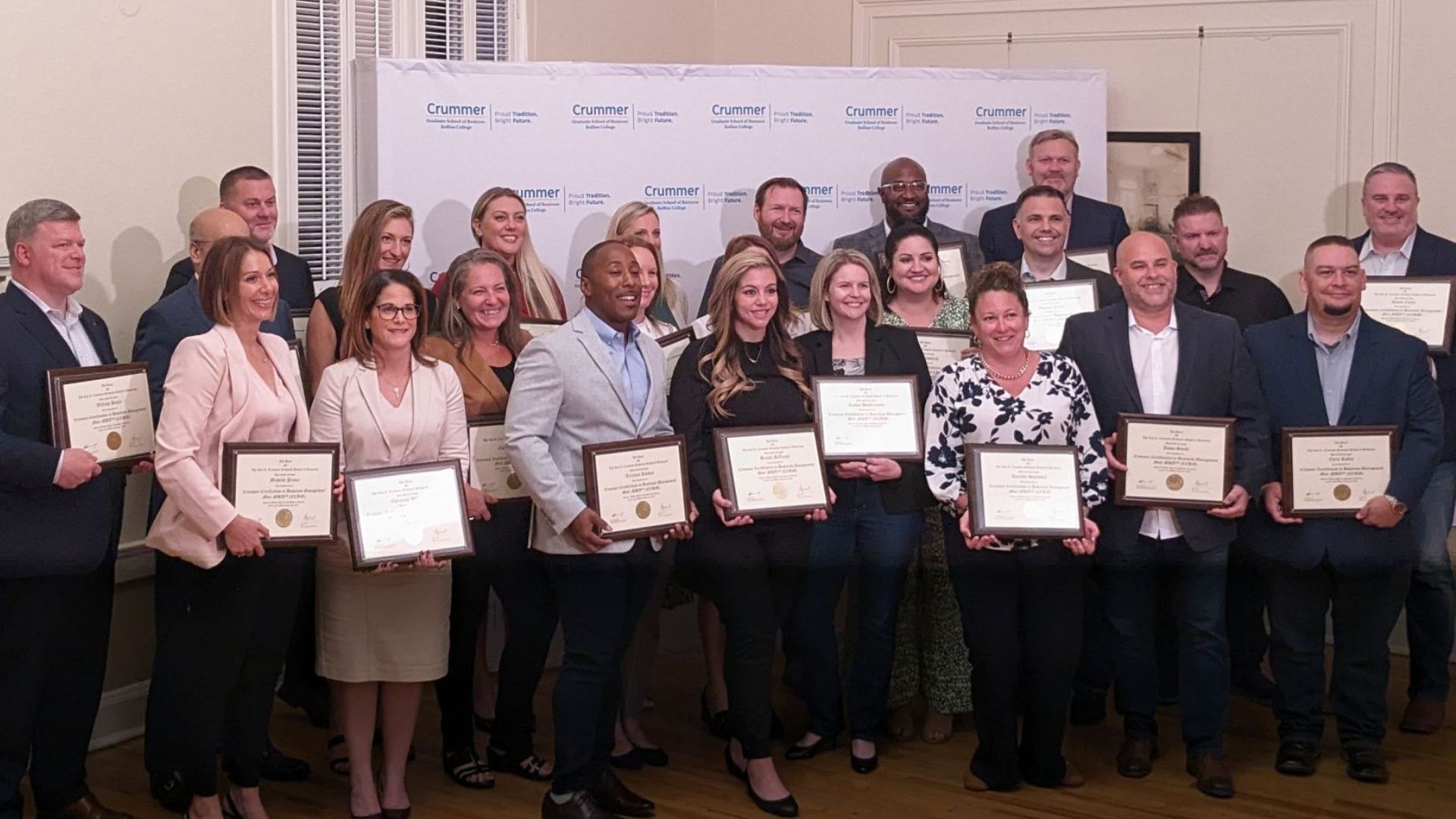 Group of Crummer Graduate School of Business certificate recipients at event stand in three rows holding their certificates