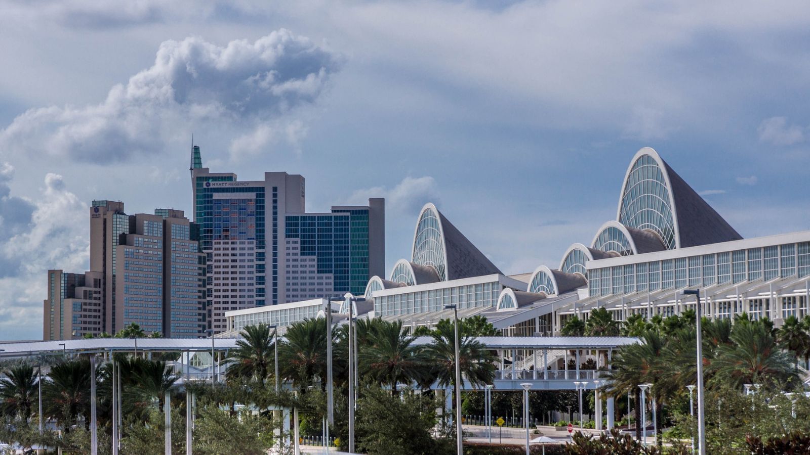 Modern glass convention center with arched roofs with Orlando skyline in the background and palm trees in the foreground