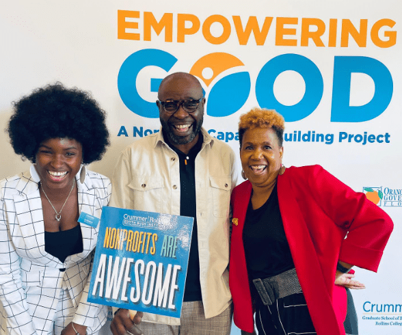 Three people smiling at Empowering Good event, middle person holding sign reading "Nonprofits are Awesome," Crummer logo visible