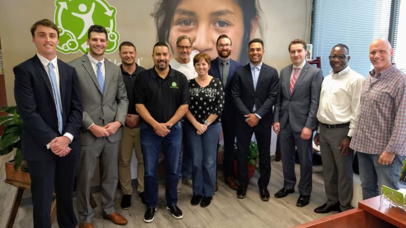 Crummer graduate business students and local business leaders smile as a group towards the camera in an indoor meeting room