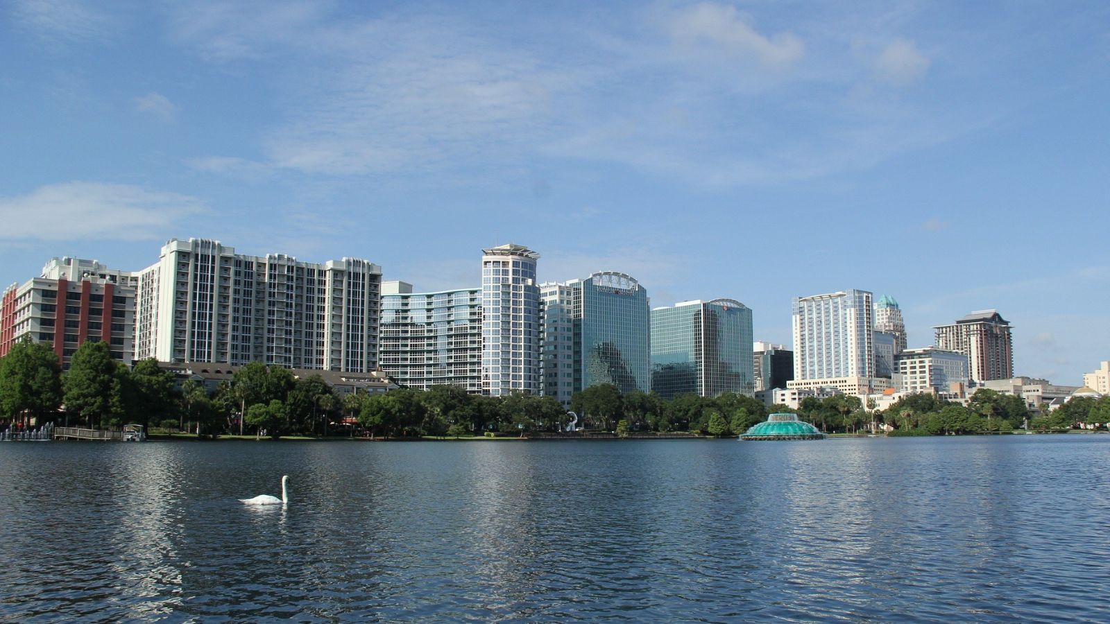 Downtown Orlando skyscrapers reflect in Lake Eola with swan, fountain, and trees visible, just ten minutes away from Crummer