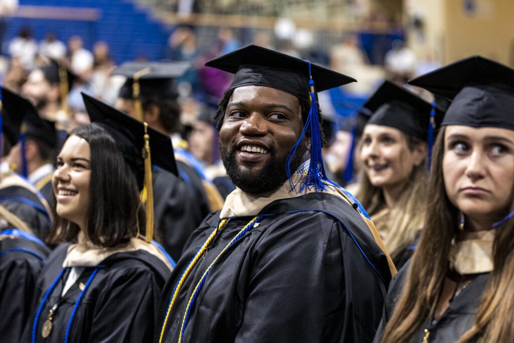 Smiling Crummer graduates wear caps and gowns with blue and gold tassels during the graduation ceremony