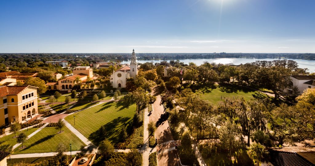 The Rollins College campus viewed from the top showcases a scenic lake, a chapel, and green space crossed by brick paths