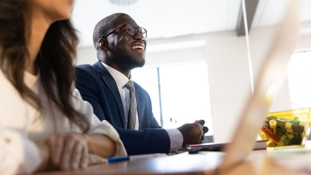 Rollins Crummer MBA student smiles during class discussion. In the foreground, another student sits with an open laptop.