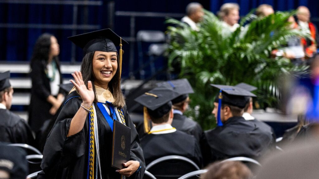 Crummer student in cap and gown waving during commencement