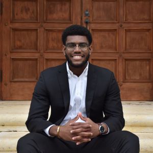 gabriel young-jack sits on stairs in front of a wooden door with his hands interlaced while smiling