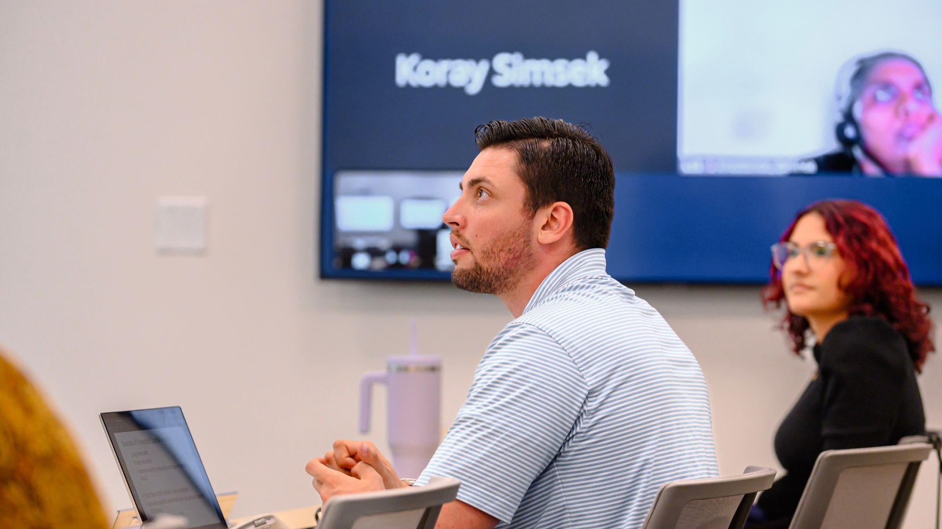 male student sits in class in front of board with student on zoom