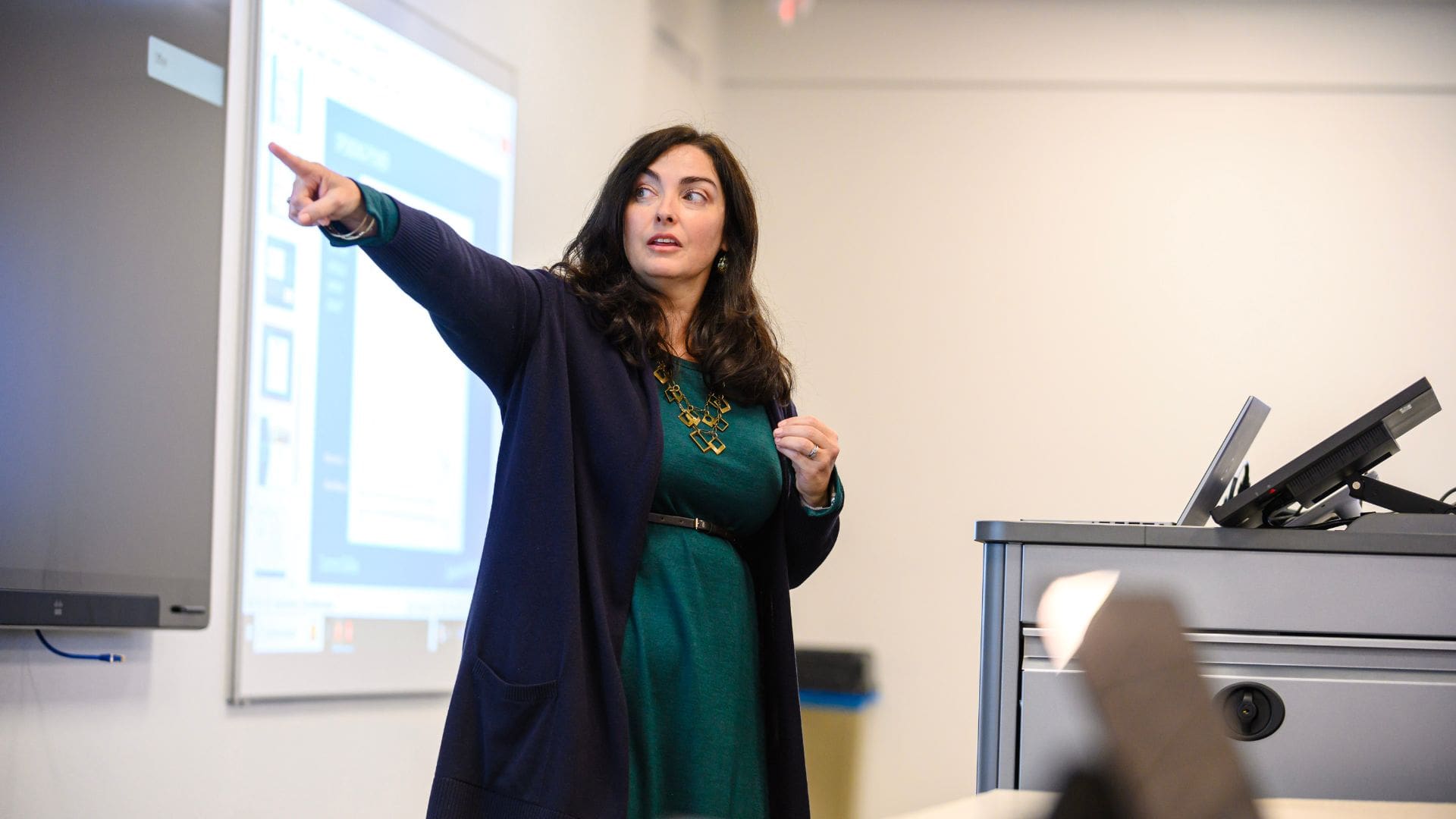 female professor in a green dress and black cardigan pointing to the board