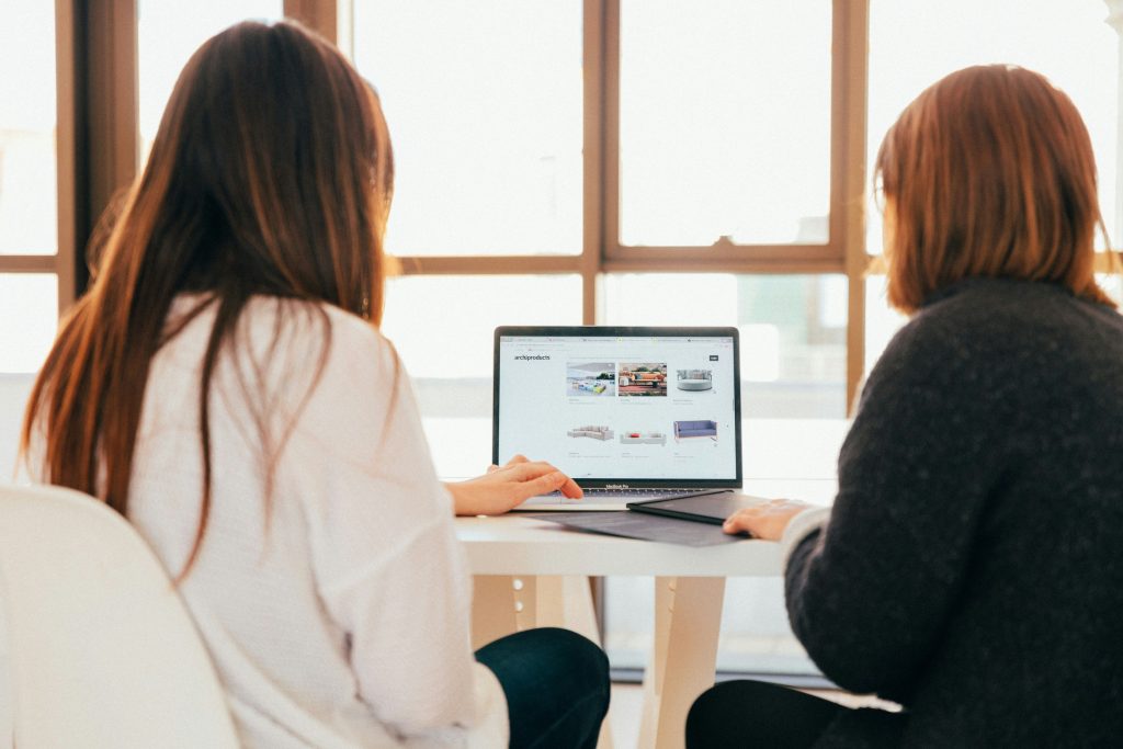Two professional women looking at a website on a laptop in a bright office.