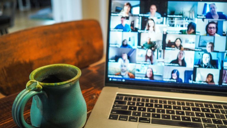 Laptop displaying a video conference next to a coffee mug.