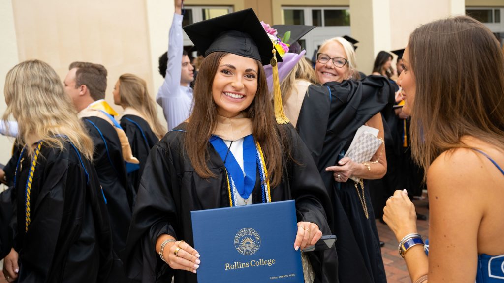 Smiling MBA graduate in a cap and gown holding her diploma.