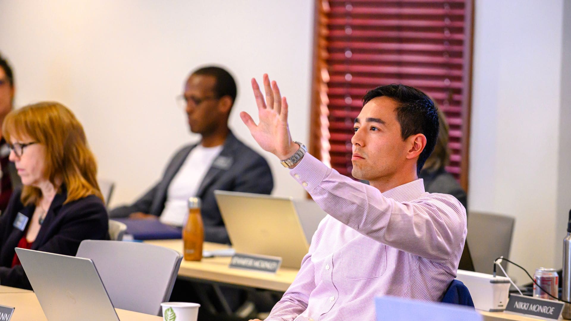 an asian male student in a pink shirt raises his hand in class