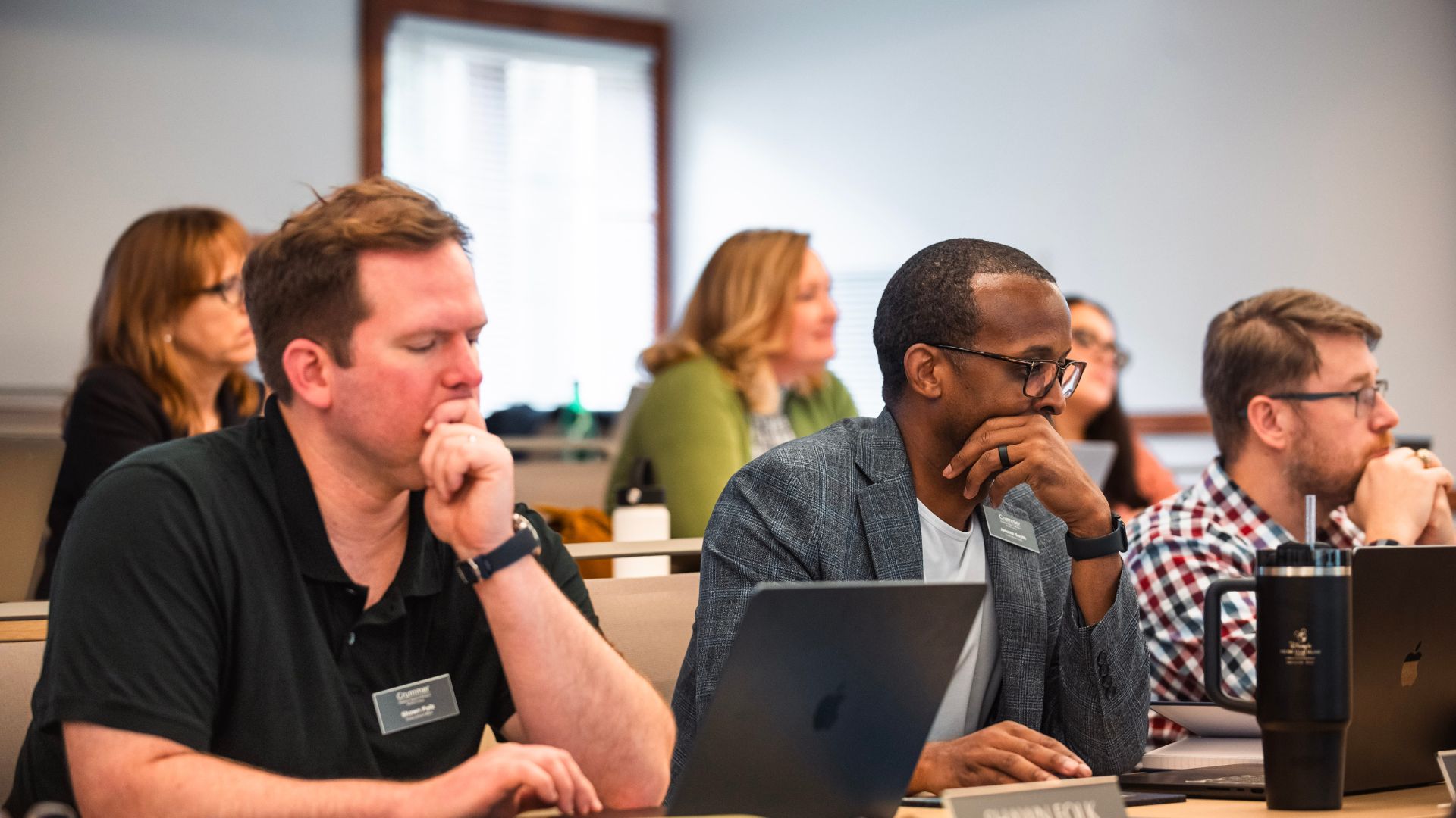 a row of male students of different races examines their laptops in class