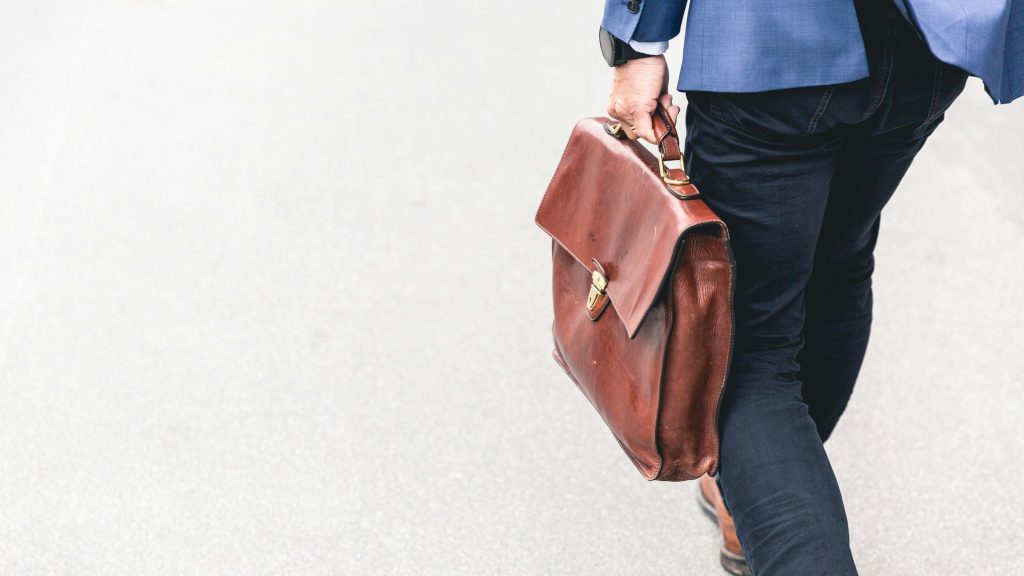 A professional man walking while carrying a leather briefcase.